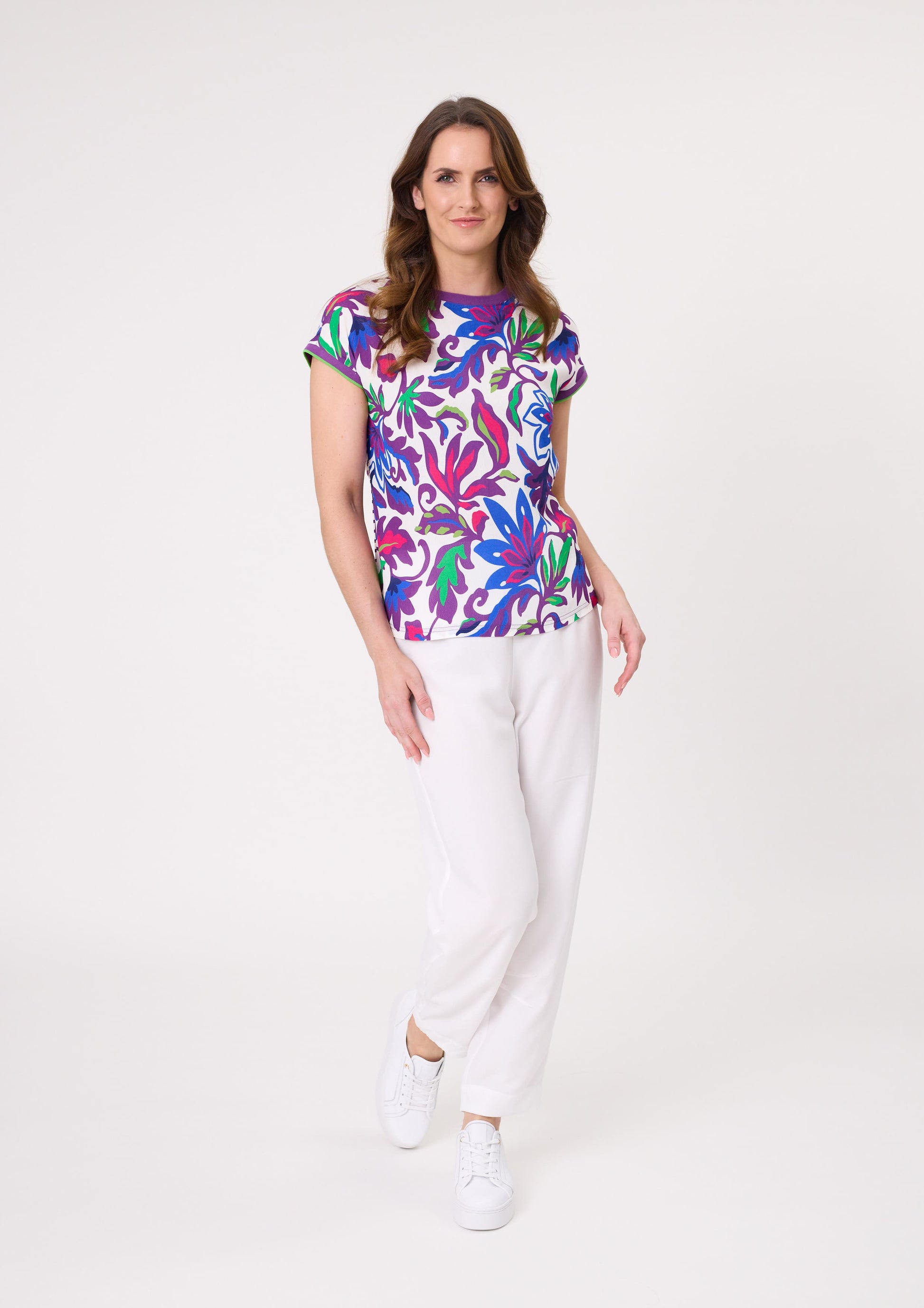 Narcisa Top with bold floral print in blue, green, purple, and cerise, featuring a round neckline and purple trim on neck and sleeves.