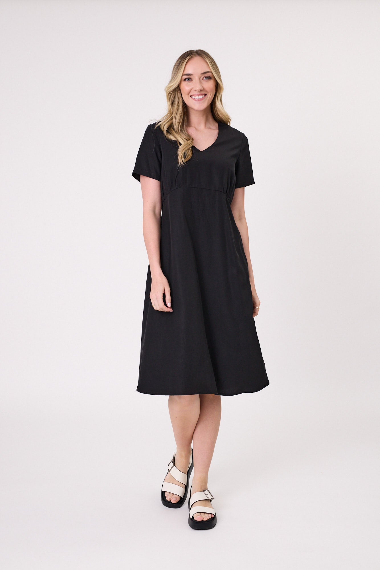Emilia Dress in black with a V-neckline, short sleeves, gentle gathers under the bust, and a knee-length silhouette, made from a soft, breathable Tencel-linen blend.