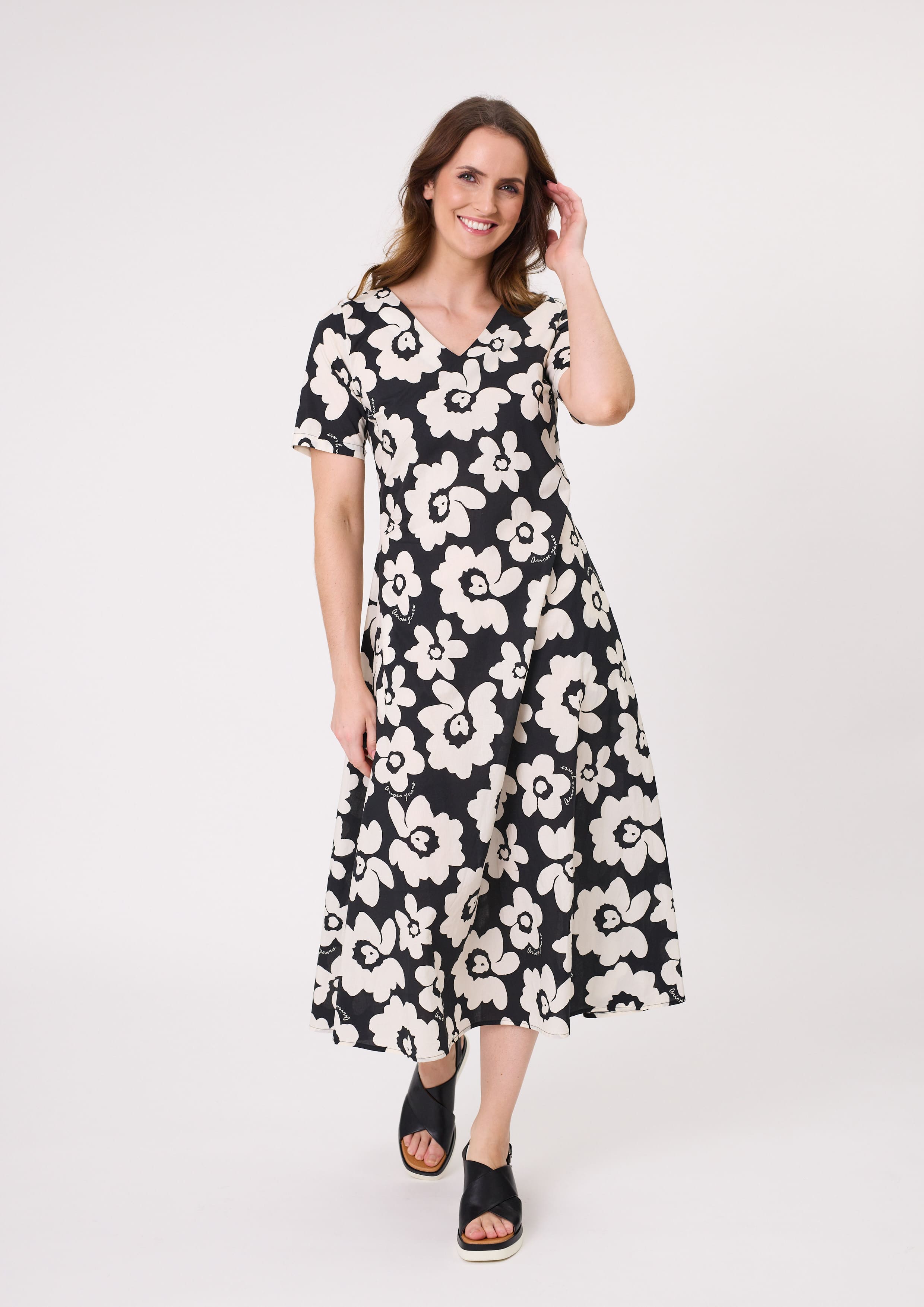 Marta Dress with a black base and white floral print, featuring a V-neckline, short sleeves, pockets, and a flattering midi length, made from 100% cotton.