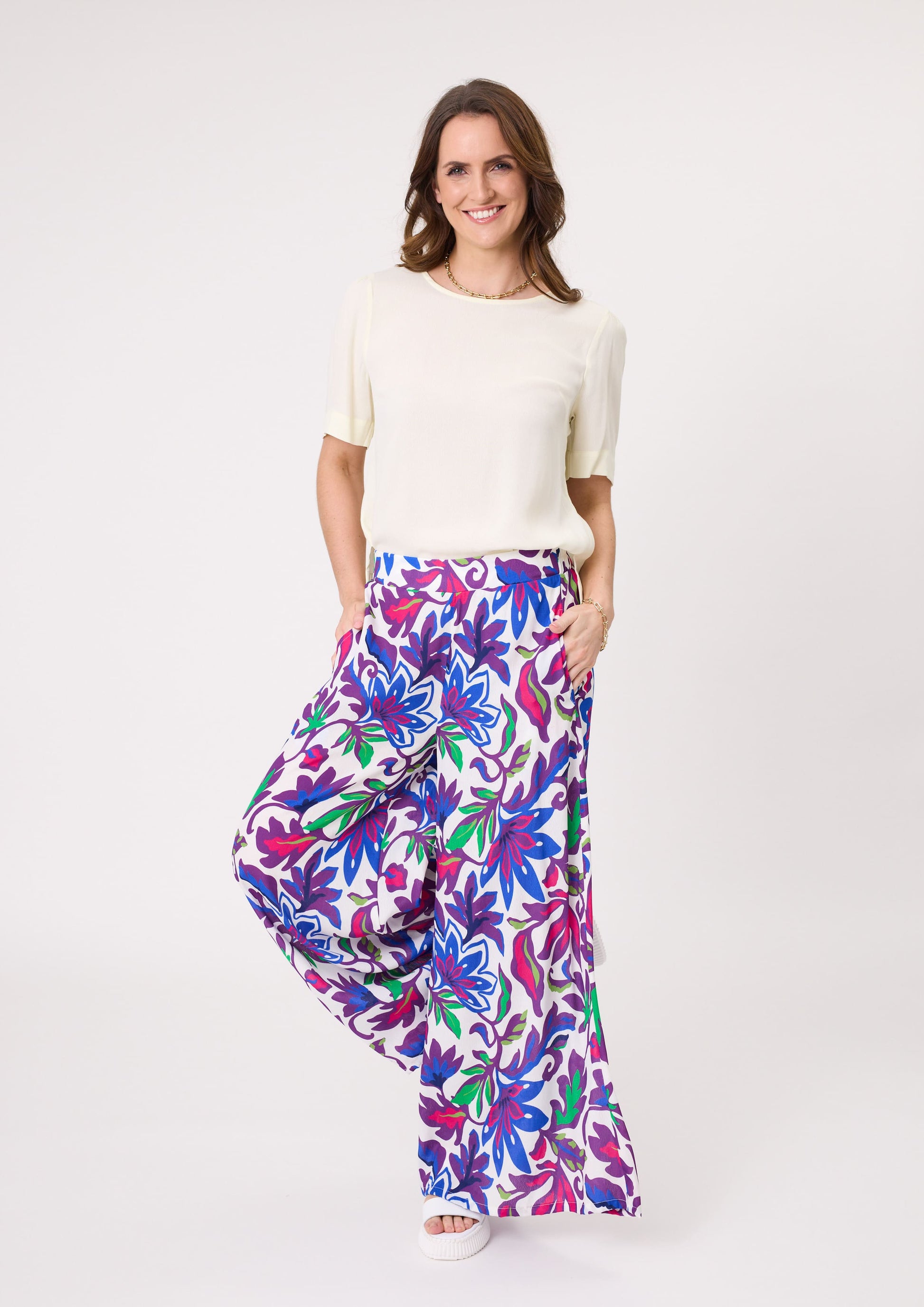 Massima Pant with bold floral print in blue, green, purple, and cerise, featuring a wide-leg silhouette, flowy drape, and practical pockets, made from a soft rayon-viscose blend.