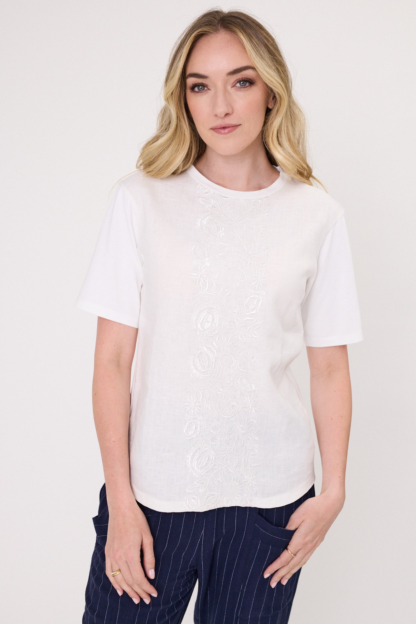 Rosetta Linen Top in white with a round neckline, short sleeves, and an embroidered floral panel down the front.